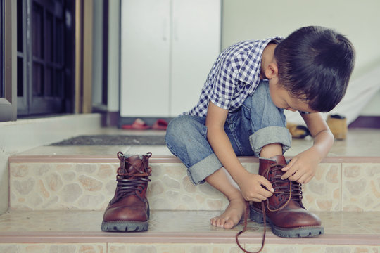 An Asian boy is trying on his father shoes.
