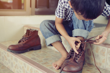 An Asian boy is trying on his father shoes.