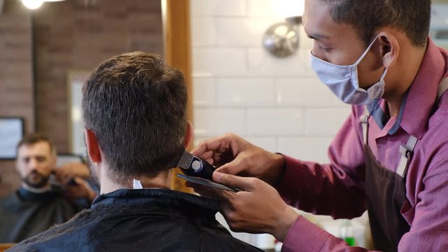 Young man getting hairstyling and haircutting in a barber shop or hair salon. Master wearing protective mask and cuts hair of men in the barbershop