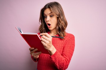 Young blonde student girl reading a book over pink  isolated background scared in shock with a surprise face, afraid and excited with fear expression