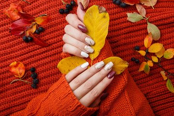 Autumn manicure. Beautyful nails design with autumn leaves. Top view. cozy autumn image. Cozy nails design. autumn leaves. Manicured woman's hands in warm wool turquoise sweater on red knit background
