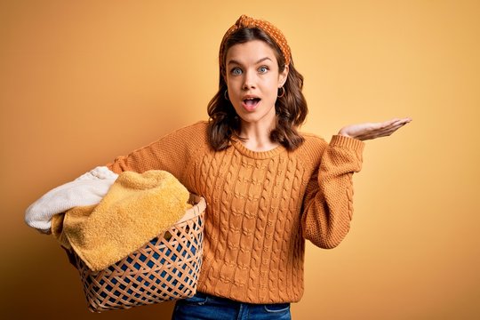 Young blonde girl doing housework chores holding laundry wicker basket very happy and excited, winner expression celebrating victory screaming with big smile and raised hands