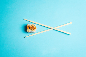 Piece of sushi between two chopsticks on a blue background
