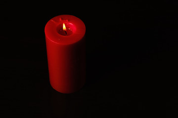 Red candle isolated on black background with a flame burning