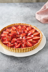Tart with strawberries and whipped cream on gray background.