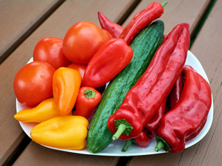Group of vegetables on a plate close-up. Mix of vegetables. Paprika, tomatoes and cucumber. Wooden table