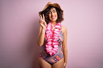 Young beautiful arab woman on vacation wearing swimsuit and hawaiian lei flowers showing and...