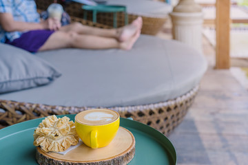 Hot coffee in a yellow cup and crispy lotus blossom cookie for relax time on wooden board at the balcony