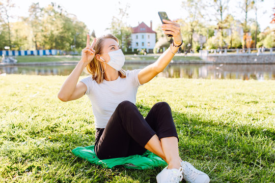 A White Woman In Face Mask While Using Her Phone For Selfie And Video Chats. The New Recommendation - Everyone To Wear Masks In Public During The Coronavirus Pandemic.