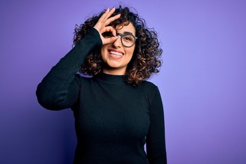 Young beautiful curly arab woman wearing casual sweater and glasses over purple background doing ok gesture with hand smiling, eye looking through fingers with happy face.