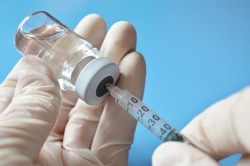 Medical professional in a rubber gloves extract a drug dose from a medical vial using a disposable...