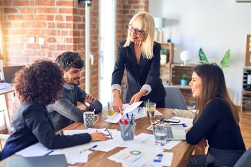 Group of business workers smiling happy and confident. Working together with smile on face. Middle age beautiful woman standing explaining documents at the office