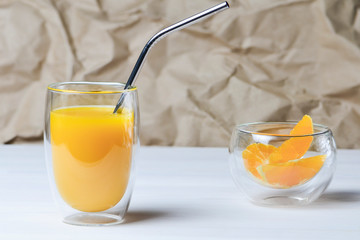 A glass of orange juice with a metal cocktail straw next to slices of orange in a transparent bowl