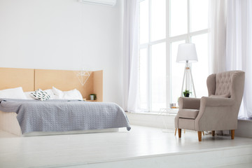 Stylish bedroom in loft style with light grey colors and wooden bed. Bed with grey blanket