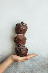 A tower of three chocolate muffins is built on the hand