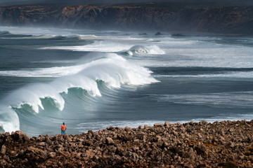 A surfer watching a set of waves breaking at the Bordeira Beach (Praia da Bordeira) in Algarve,...