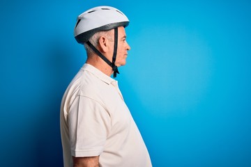 Middle age hoary cyclist man wearing bike security helmet over isolated blue background looking to side, relax profile pose with natural face with confident smile.
