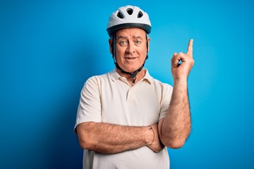 Middle age hoary cyclist man wearing bike security helmet over isolated blue background with a big...