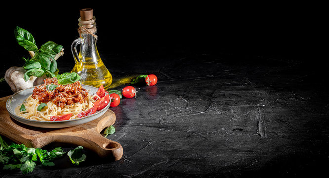 Heaped plate of delicious Italian spaghetti pasta with fresh basil leaves and grated parmesan cheese on dark background