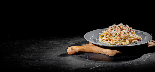 Delicious Italian spaghetti pasta with salmon, fresh basil leaves and grated parmesan cheese on dark background