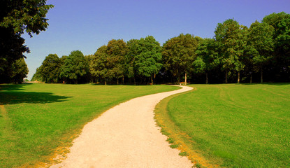 narrow sepia colored path in the green park with smooth summer sky above