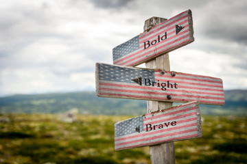 Bold bright and brave text on wooden american flag signpost outdoors in nature.