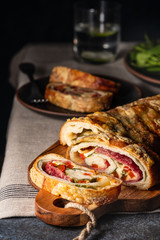 Traditional Italian Stromboli stuffed with cheese, salami, red pepper and spinach. Photo in a dark style.