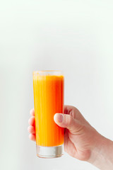 Hand holding glass of carrot juice. Fresh juice on glass isolated on white background.