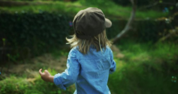 Preschooler with hat seeing bubbles in garden and chasing them