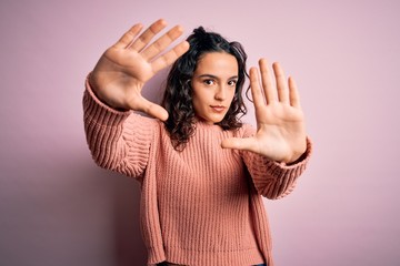 Young beautiful woman with curly hair wearing casual sweater over isolated pink background doing frame using hands palms and fingers, camera perspective