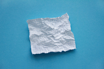 Crumpled square white checked paper sheet on on blue background 