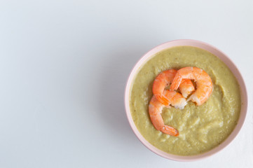broccoli soup with king prawns in a pink bowl on a white background