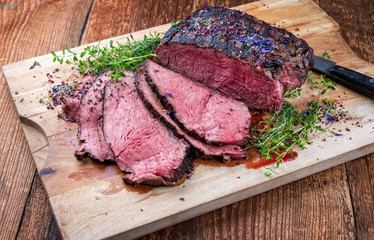 Traditional Commonwealth Sunday roast with sliced cold cuts roast beef with herbs and salt as closeup on a rustic wooden cutting board