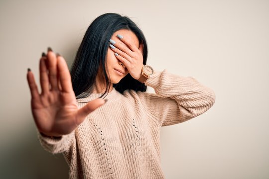 Young beautiful chinese woman wearing casual sweater over isolated white background covering eyes with hands and doing stop gesture with sad and fear expression. Embarrassed and negative concept.