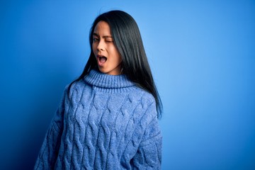 Young beautiful chinese woman wearing casual sweater over isolated blue background winking looking at the camera with sexy expression, cheerful and happy face.