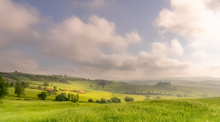 Fototapeta na wymiar Green landscape with clouds. Early May morning in San Quirico D'orcia, Tuscany - Italy.
