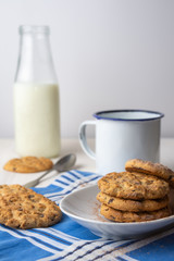 Fototapeta na wymiar Close-up of chocolate chip cookies on white plate with cup, spoon and bottle of milk on blue napkin, with selective focus, white background, vertical