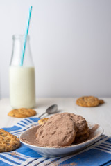 close-up of plate of chocolate powder cookies, bottle of milk with straw, on blue napkin and white background, vertical