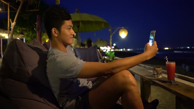 Young man with cocktail taking selfie with cellphone at beach bar