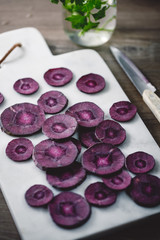 Slices of purple carrot on a white marble board over kitchen table.