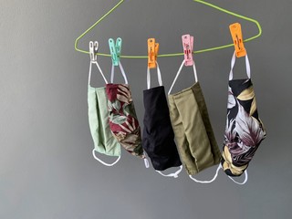 Reusable fabric face masks hang on clothes hanger with grey background 