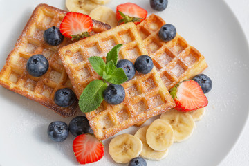 Delicious waffles with blueberries, strawberries and bananas. Plate with tasty waffles. Close up