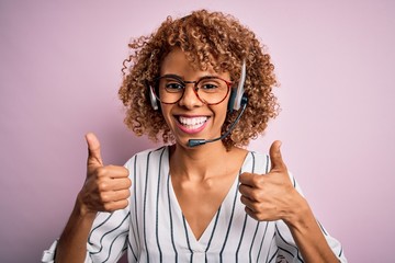African american curly call center agent woman working using headset over pink background success...