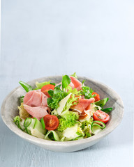 Salad with ham, vine tomatoes, parmesan cheese, prosciutto and green mix over light blue background with copy space. Close up. Healthy food concept.
