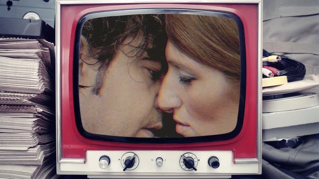 Two lovers on a vintage tv: a woman faking a kiss, halting it, a man saddened by the unexpected end.
