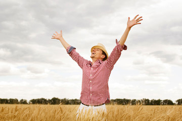 Young handsome happy man standing in wheat field spreading his arms up 