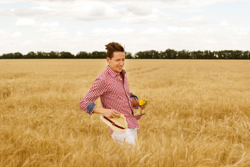 Young handsome happy man with sunflower in hands standing in wheat field 