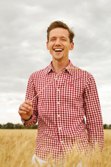 Young handsome happy man standing in wheat field 