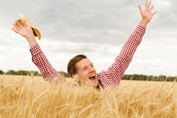 Young handsome happy man standing in wheat field spreading his arms up 
