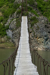 Suspension bridge over a small river in a mountainous countryside on a sunny summer day. Traveled photo in Russia.